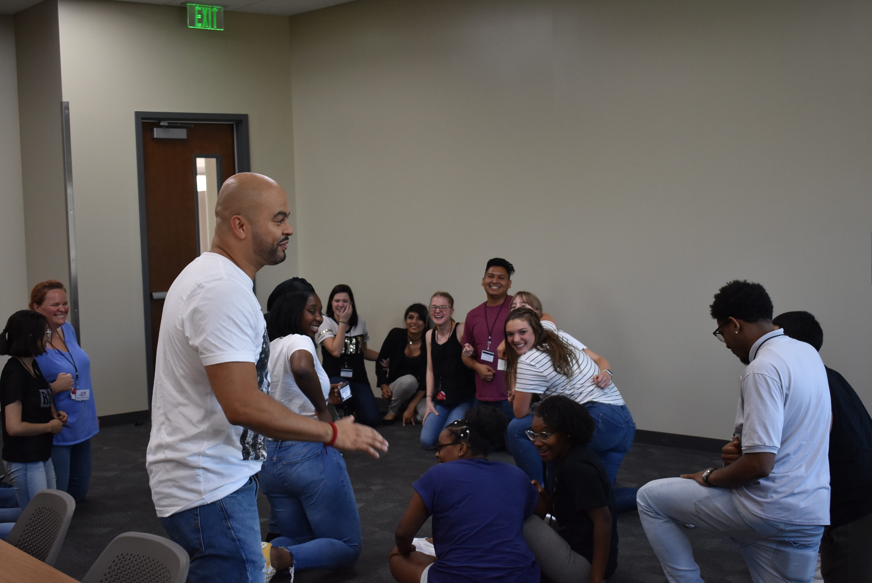 A man in a white shirt and jeans wears a bemused expression as he leads a group of young people through a teambuilding exercise.