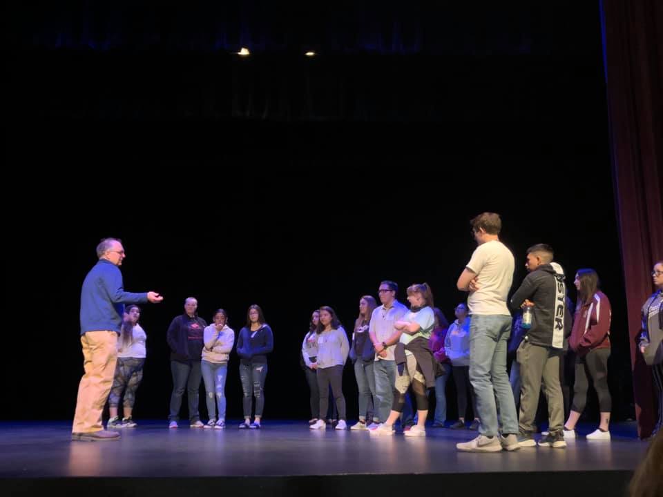 Workshop participants on a stage gather in a semi-circle around a speaker